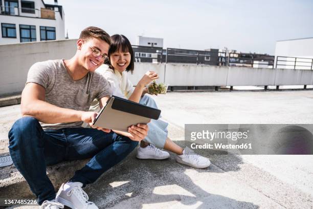 smiling male and female friends using digital tablet on sunny day - male teen tablet stock-fotos und bilder