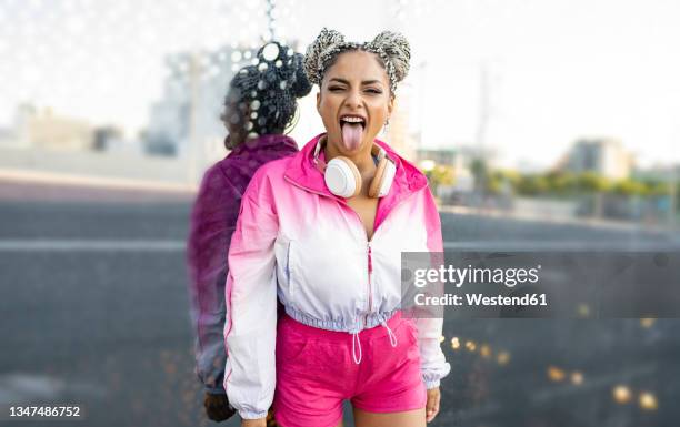 woman sticking out tongue in front of glass wall - haarknoten stock-fotos und bilder