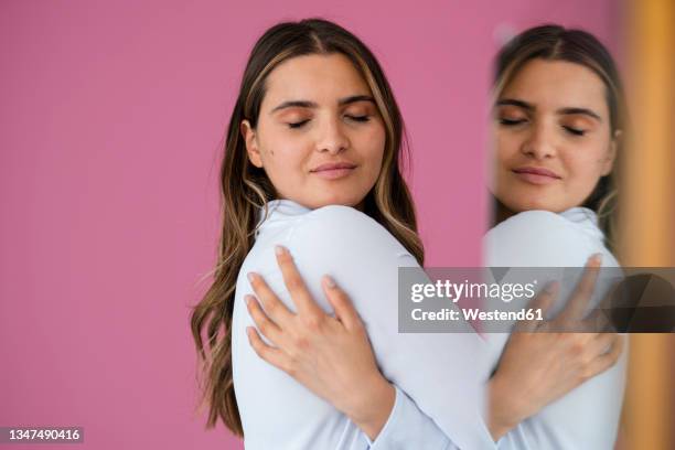 businesswoman hugging herself by pink wall - hugging self stock-fotos und bilder