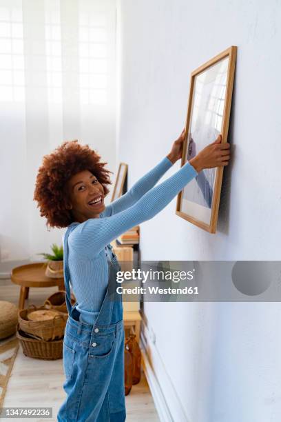 happy woman adjusting picture frame on white wall - draped fotografías e imágenes de stock