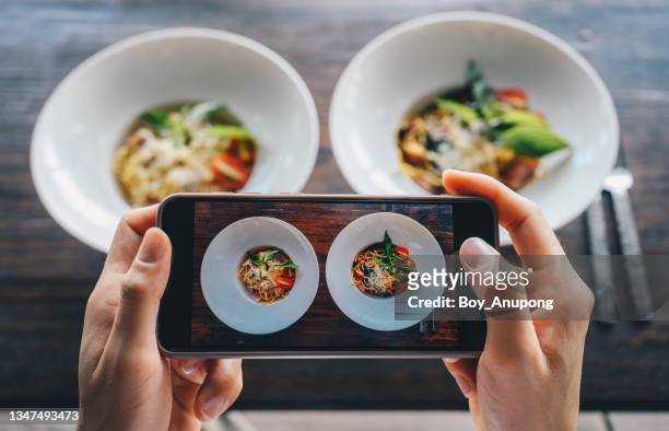 cropped shot of woman hands taking photo of spaghetti with mobile phone in restaurant for post on social media before eating. - holding two things stock pictures, royalty-free photos & images