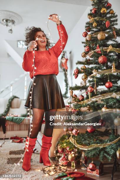 femmina sorridente che si diverte a decorare l'albero di natale con le luci a casa - decorare l'albero di natale foto e immagini stock