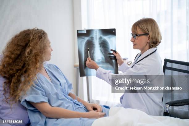 mature female doctor checking x-ray with female mature patient in patient room. - lung doctor patient stockfoto's en -beelden