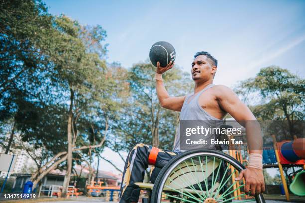 disabled asian indian man in wheelchair practicing with medicine ball in public park morning routine - medicine ball stockfoto's en -beelden