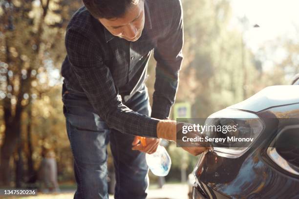 man wipes headlight of car - abrillantar fotografías e imágenes de stock