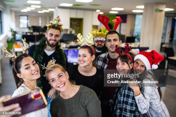coworkers taking selfies at the office christmas party - christmas party stockfoto's en -beelden