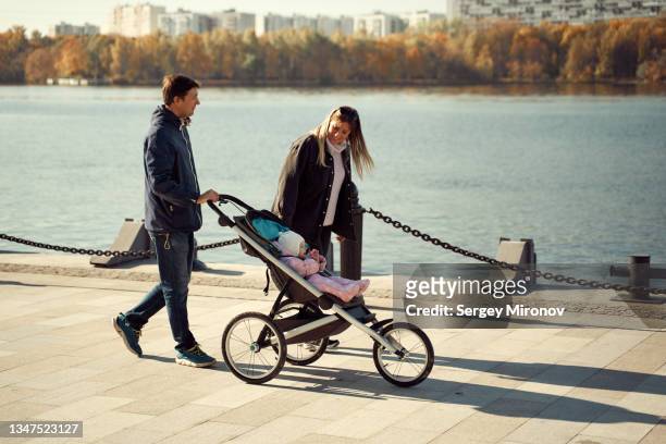 couple walking with baby in baby carriage on boardwalk - baby stroller stock-fotos und bilder