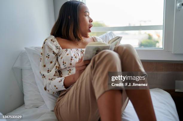 woman with book in bed yawning - j lee fotografías e imágenes de stock