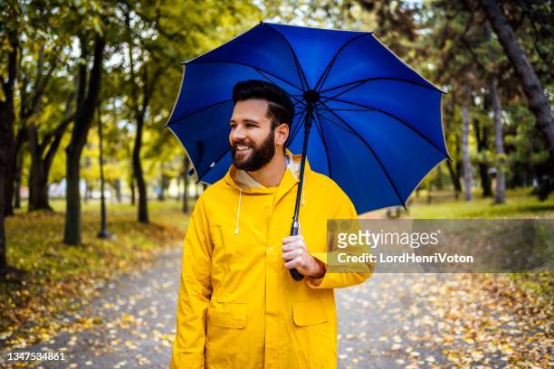 lächelnder mann mit blauem regenschirm - raincoat stock-fotos und bilder