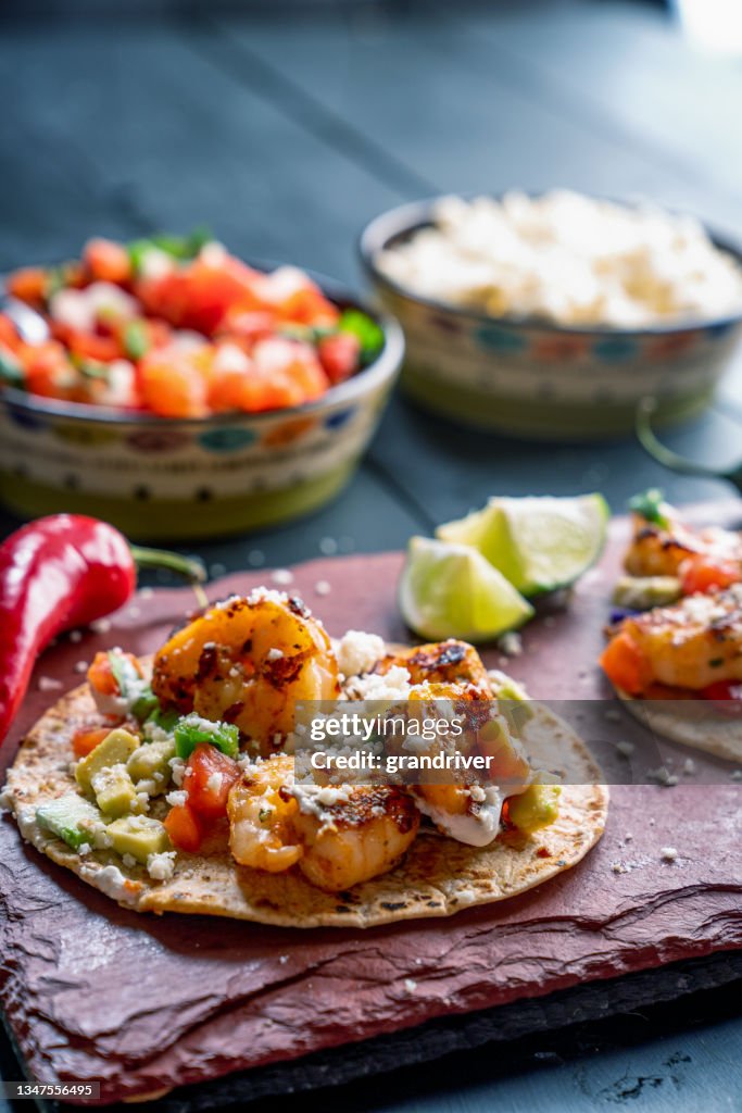 A Platter With Three Gourmet Shrimp Tacos With A Bowls Of Cotilla Cheese And Fresh Salsa