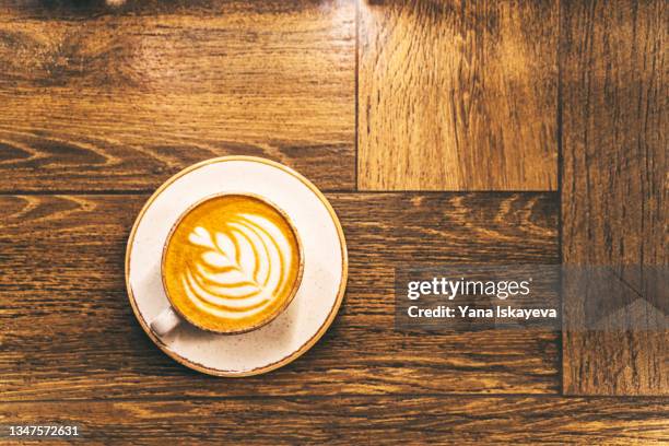 a hot cup of cappuccino with rosetta latte art on a dark wooden surface or table - mesa de café - fotografias e filmes do acervo