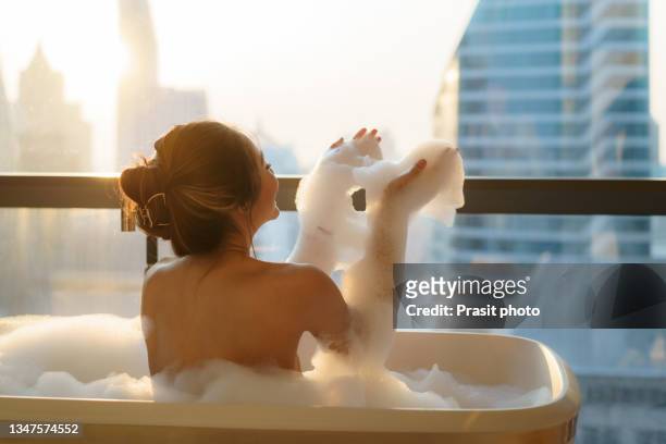 asian woman takes a bath with soap bubble in bathtub at bathroom of luxury hotel in downtown city while on vacation. - women taking showers stock pictures, royalty-free photos & images