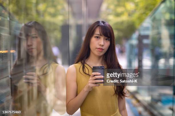 portrait of japanese woman in yellow dress leaning on glass wall in city - beige dress stock pictures, royalty-free photos & images
