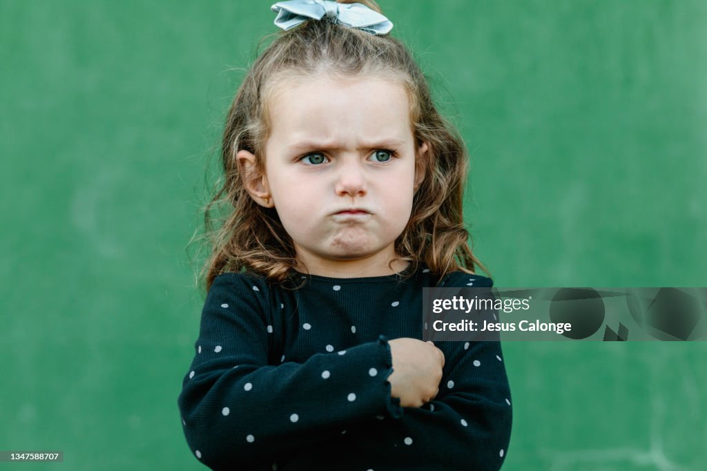 Portrait of a Caucasian girl, with a anger and annoyance expression. With a street wall in the background. Children, psychology, education and free time concept.