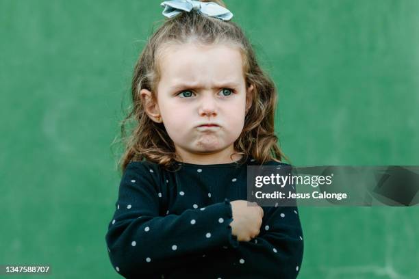 portrait of a caucasian girl, with a anger and annoyance expression. with a street wall in the background. children, psychology, education and free time concept. - angry babies stock pictures, royalty-free photos & images