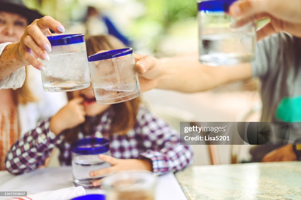 Family clink glasses and cheers each other with water glasses at an outdoor restaurant
