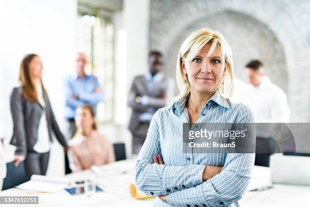 donna d'affari con le braccia incrociate davanti ai suoi colleghi in ufficio. - persona in secondo piano foto e immagini stock