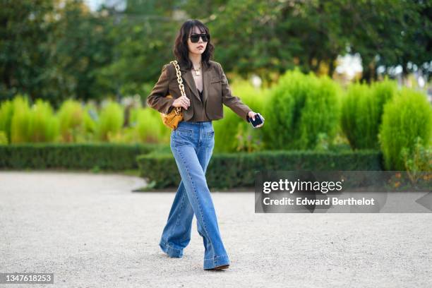 Xiayan wears black sunglasses, a gold large chain necklace, a black V-neck ruffled cropped tank-top, silver rings form Hermes, a brown matte leather...