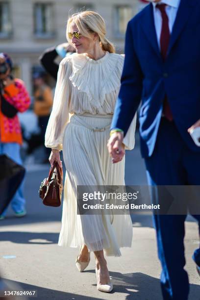 Gillian Anderson wears sunglasses, gold pendant earrings, a white ruffled tulle / large collar / puffy sleeves / midi flowing dress, a white latte...