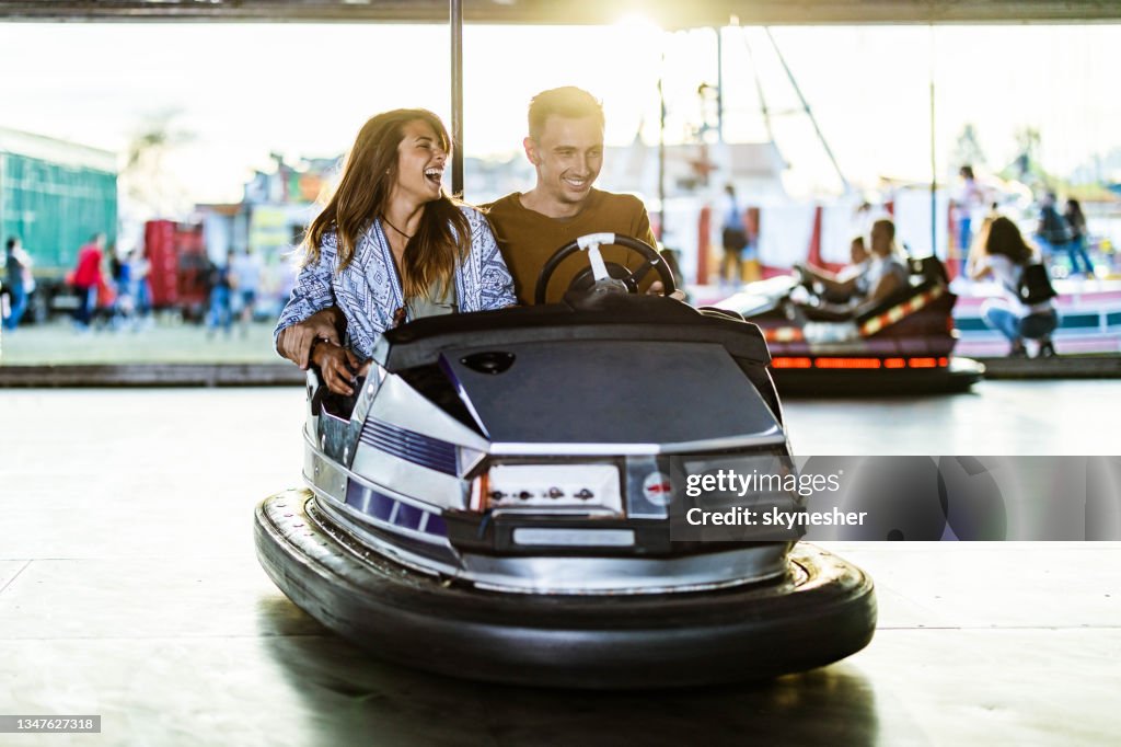 Young happy couple having fun in bumper car at amusement park.