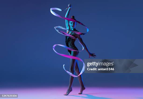 plan de studio d’une petite fille, artiste de gymnastique rythmique isolée sur fond de studio bleu dans un néon rose. - visage danseuse photos et images de collection