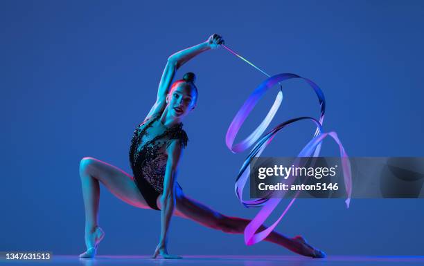 studio shot of little girl, rhythmic gymnastics artist isolated on blue studio background in pink neon light. - rhythm stock pictures, royalty-free photos & images