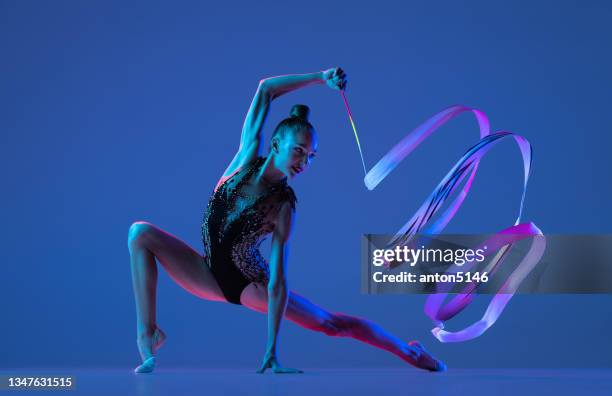 studioaufnahme eines kleinen mädchens, einer künstlerin der rhythmischen gymnastik, isoliert auf blauem studiohintergrund in rosa neonlicht. - ribbon dance stock-fotos und bilder