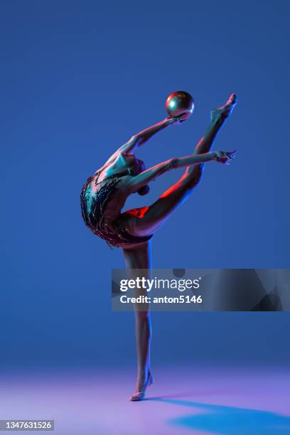 one young girl, rhythmic gymnastics artist in bright beautiful sports costume isolated on blue studio background in neon. - gymnastiek stockfoto's en -beelden