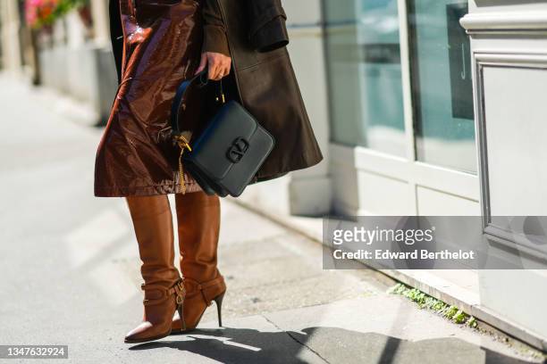 Elisa Taviti wears a brown shiny leather long coat, a black shiny leather handbag from Valentino, a high waist brown shiny leather / vinyl slit /...
