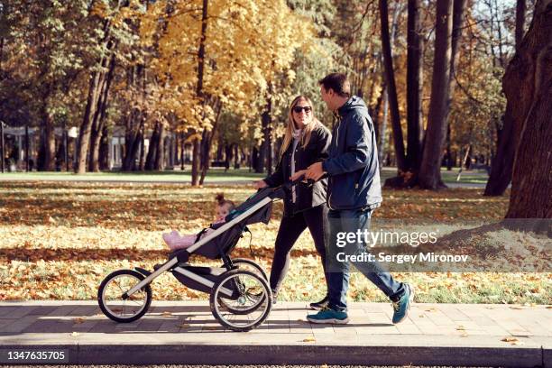 young couple walking with baby in baby carriage on park - baby pram in the park stock-fotos und bilder