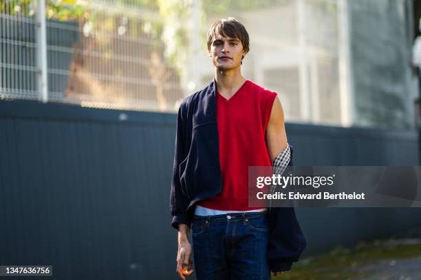 Guest wears a red wool sleeveless pullover, a navy blue wool coat with checkered pattern interior, navy blue denim jeans large pants, outside...