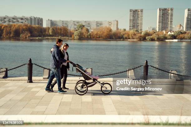 couple walking with baby in baby carriage on embankment - emerald city stockfoto's en -beelden