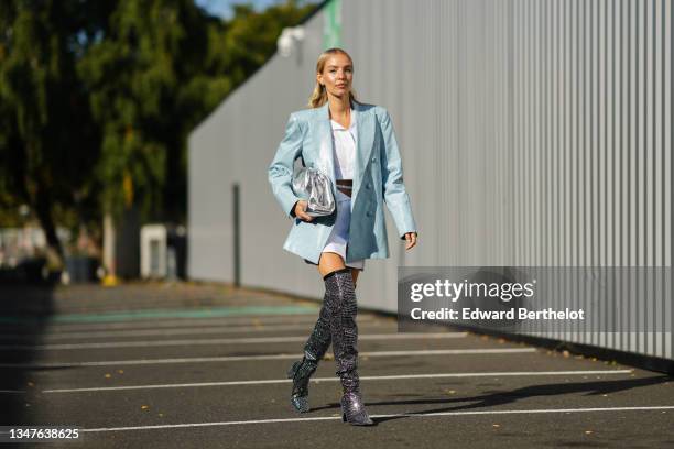 Leonie Hanne wears a silver and rhinestones earring from Chanel, a white cropped shirt, a white leather belt, a white buttoned wrap short skirt, a...
