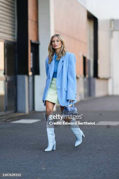 Xenia Adonts wears large silver earrings, a blue ribbed t-shirt, a pale yellow denim short skirt, a pale / baby blue oversized blazer jacket, a blue...