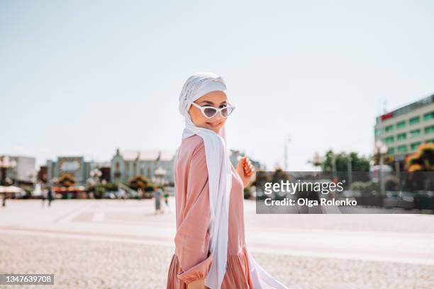 young muslim woman dressed in traditional pink dress walks down the street on a summer day - anständig klädsel bildbanksfoton och bilder