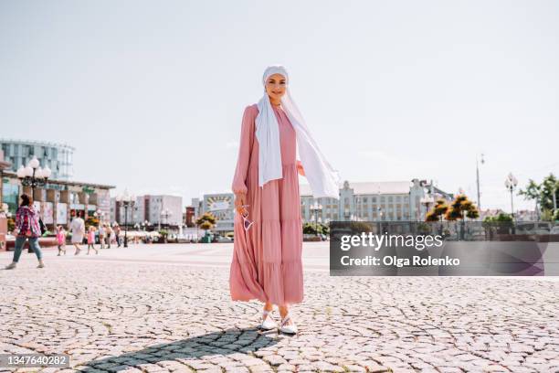 young muslim woman dressed in traditional pink dress walks down the street on a summer day - middle eastern women foto e immagini stock