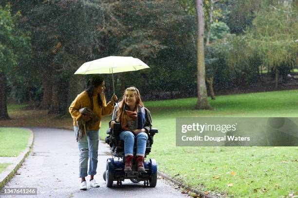 disabled woman and friend under umbrella in autumn park. - an evening with suggs friends in aid of pancreatic cancer uk stockfoto's en -beelden