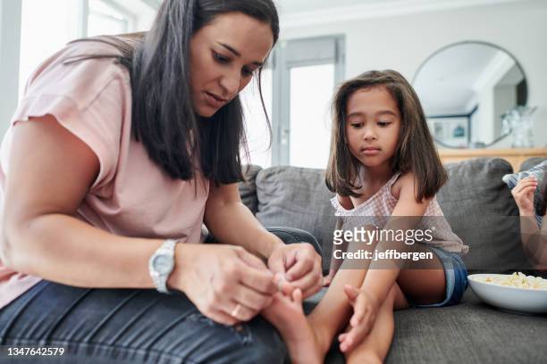 foto de una joven madre aplicándole una curita a la herida de su hija en casa - latina legs fotografías e imágenes de stock
