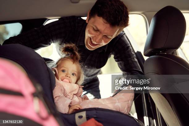 father fasten belt baby girl to car chair - fastening stock-fotos und bilder