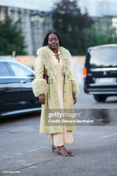 Guest wears a gold and rhinestones pendant earrings, a white pearls necklace, gold chain necklaces, a pale yellow ribbed buttoned V-neck long midi...