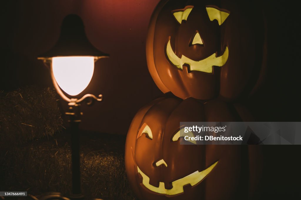 Lamppost lit up at night with a Jack-o-Lantern pumpkin lit up on the other side in a dark and mysterious setting. Concept of fear and celebration of Halloween and carnival