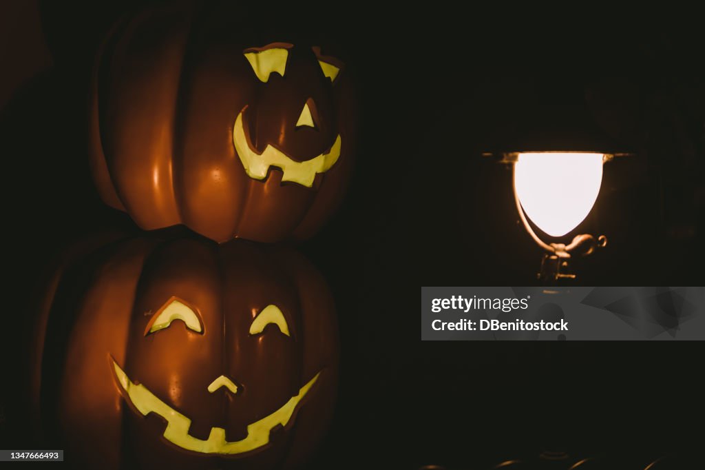 Lamppost lit up at night with a Jack-o-Lantern pumpkin lit up on the other side in a dark and mysterious setting. Concept of fear and celebration of Halloween and carnival