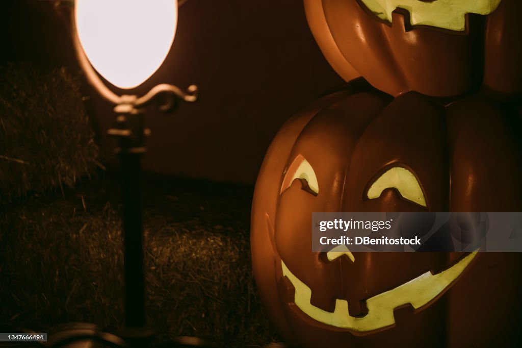 Lamppost lit up at night with a Jack-o-Lantern pumpkin lit up on the other side in a dark and mysterious setting. Concept of fear and celebration of Halloween and carnival
