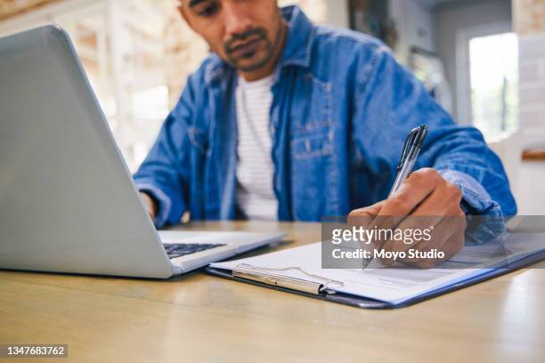 shot of a young man using a laptop and going through paperwork at home - man signing paper stock pictures, royalty-free photos & images