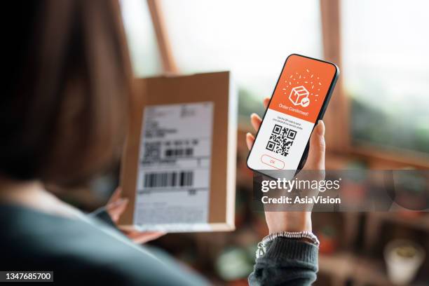 小包を持っている若いアジアの女性の肩の上に、自宅でスマートフォンにモバイルアプリで配達サービスを注文します。あなたの玄関先でピックアップと配達サービス - 宅配便サービス ストックフォトと画像