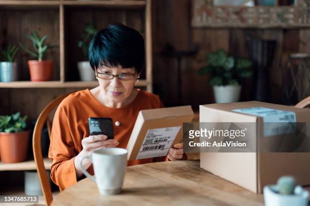 senior asian woman relaxing at home, shopping online with smartphone, receiving delivered parcels by home delivery service. online shopping, online banking. enjoyable customer shopping experience - returning product stock pictures, royalty-free photos & images