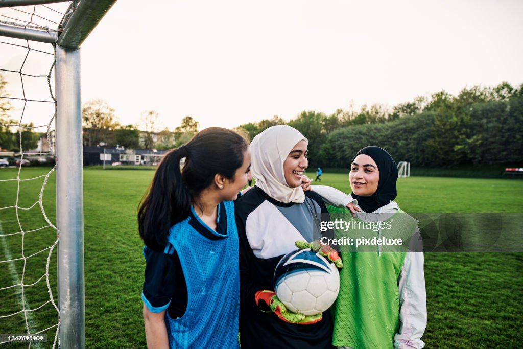 Cropped shot of three athletic young female footballers standing on a soccer pitch with their teammates in the background