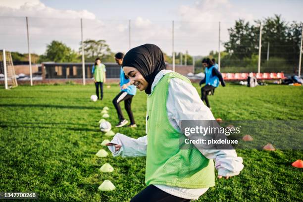 foto recortada de una joven futbolista atlética entrenando en el campo con sus compañeros de equipo en el fondo - football training fotografías e imágenes de stock