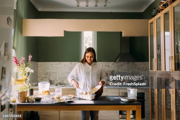 smiling overweight professional female baker pouring dough over into a baking mould - baking competition stock pictures, royalty-free photos & images