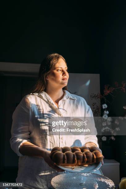 schöner lächelnder übergewichtiger bäcker, der einen teller mit süßem brot hält und wegschaut - looking back stock-fotos und bilder